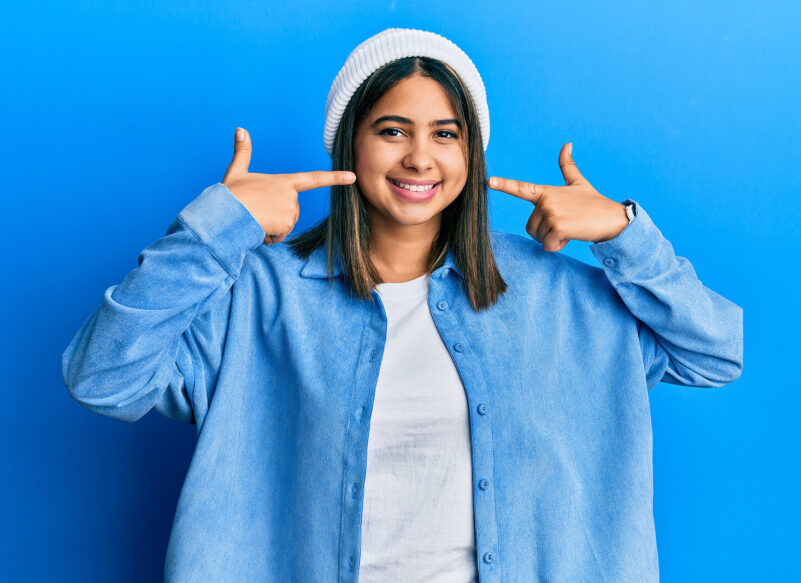 smiling woman wearing blue pointing to her teeth